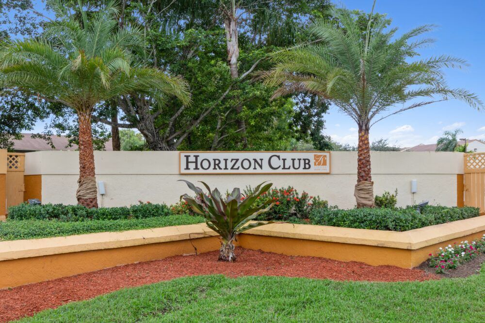 Entrance sign to Horizon Club surrounded by greenery and palm trees.