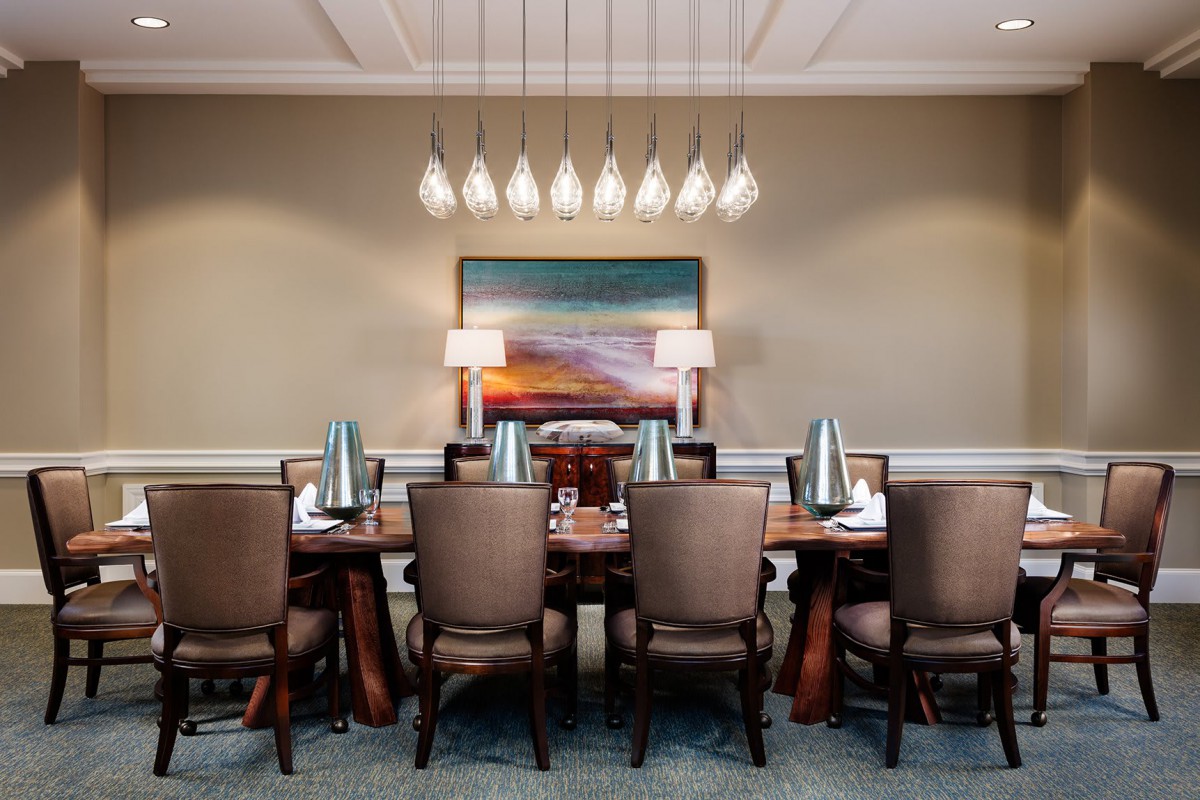 A sophisticated dining room featuring a long table with chairs, modern lighting fixtures, and a large painting on the wall.
