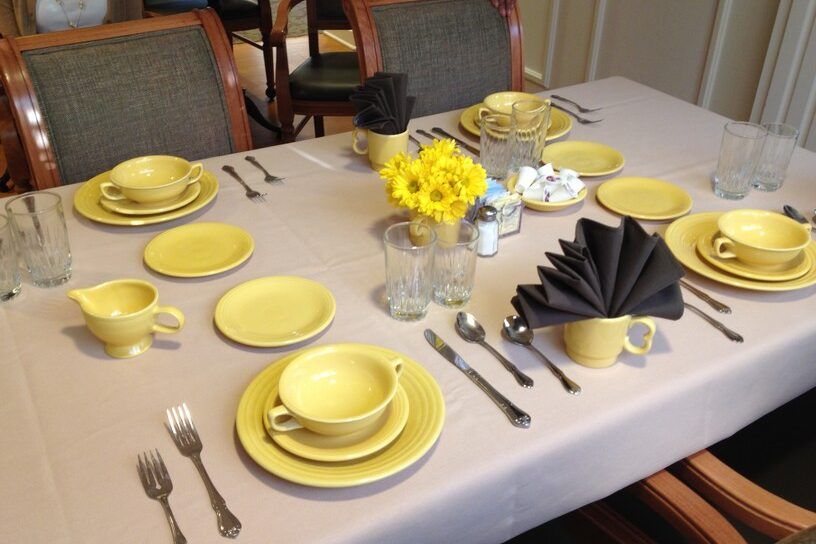 A neatly arranged dining table with yellow dishes, black napkins, and a floral centerpiece.