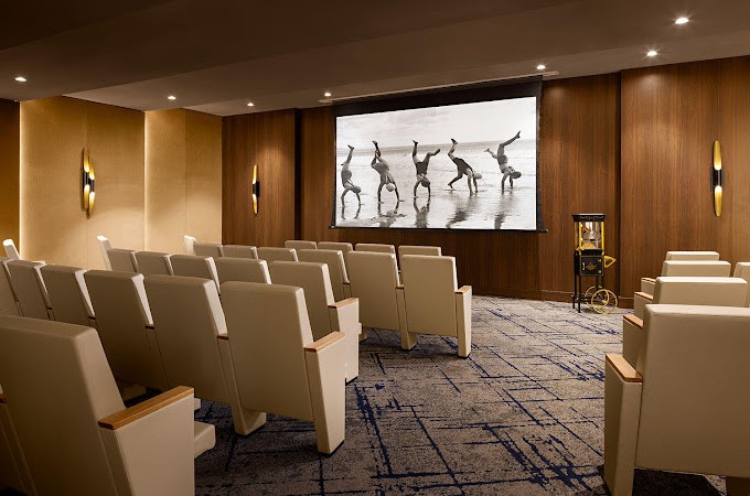 A modern cinema room with comfortable seating and a large screen displaying a black-and-white image.