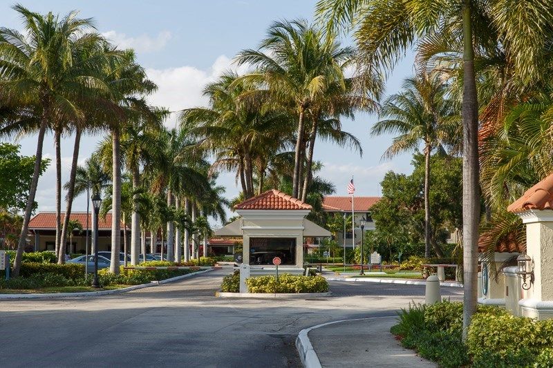 Entrance to a gated community with palm trees and a guardhouse.