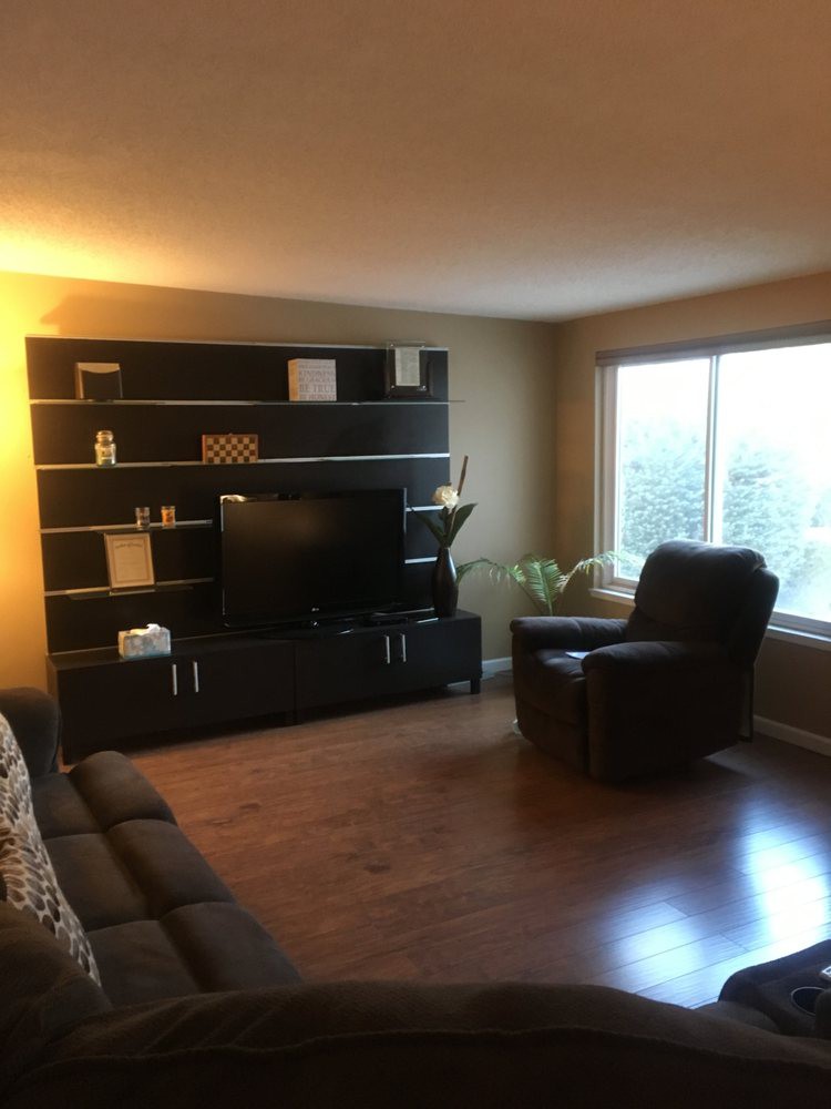 A cozy living room with a TV stand, recliner, and sofa, featuring hardwood floors and ambient lighting.
