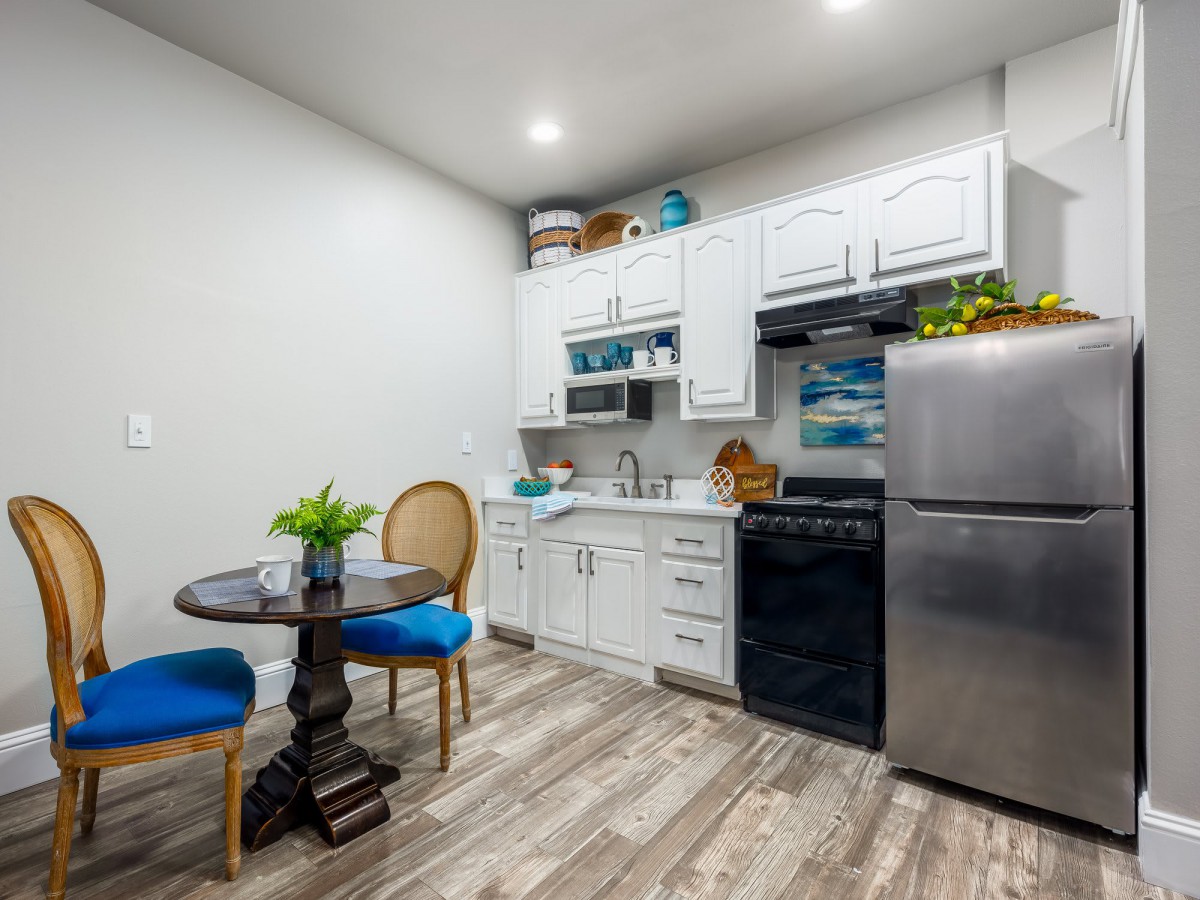 A modern apartment kitchen with white cabinets, stainless steel appliances, and a small dining area.
