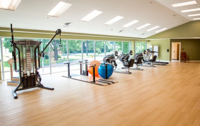 A spacious gym with various exercise equipment and large windows providing natural light.
