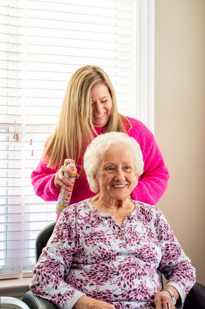 A caregiver happily brushes the hair of an elderly woman indoors.