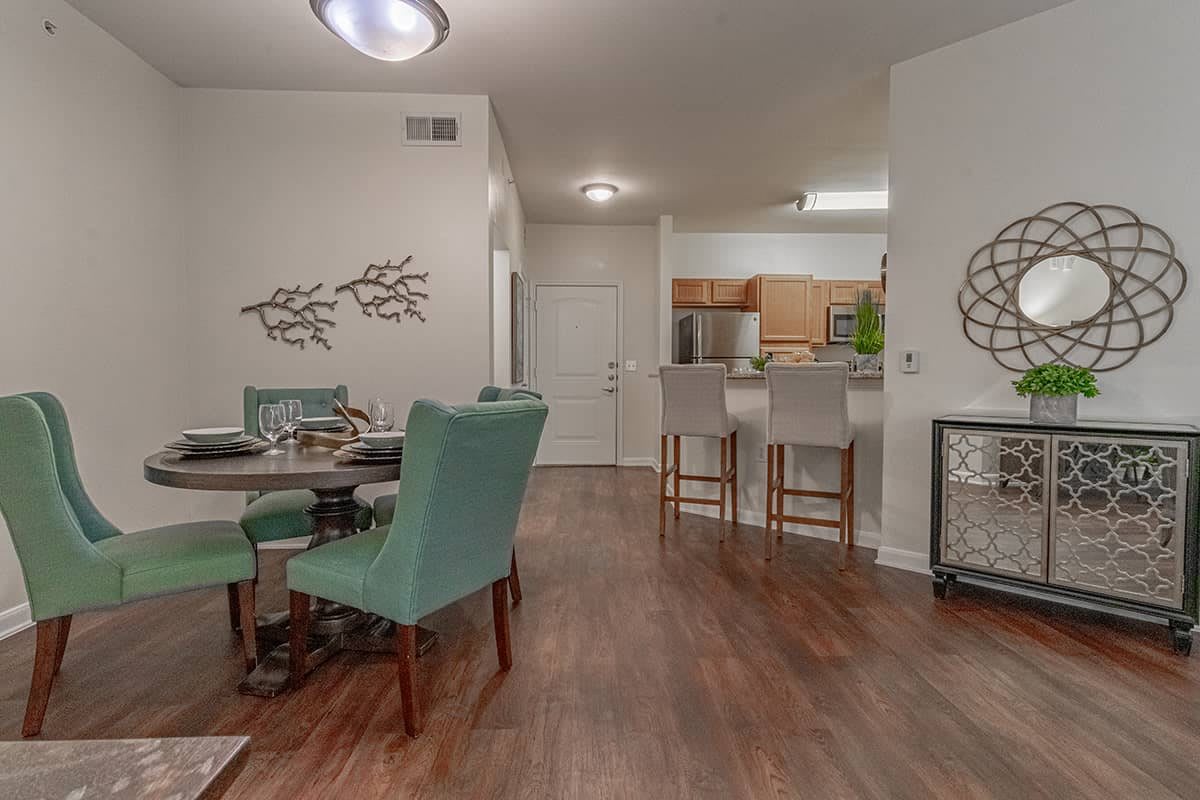 A modern open-concept living space featuring a dining area with turquoise chairs and a kitchen with bar seating.