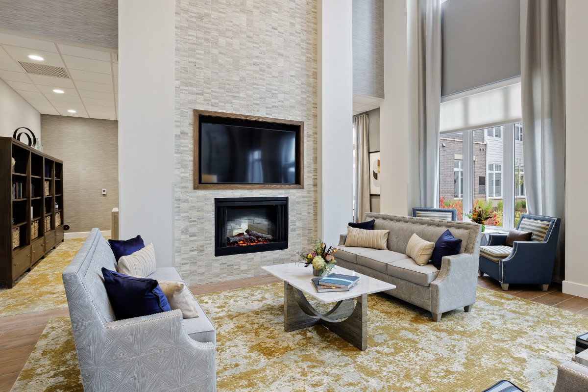 A spacious modern living room featuring a stone fireplace, wall-mounted television, and elegant sofas with decorative pillows.