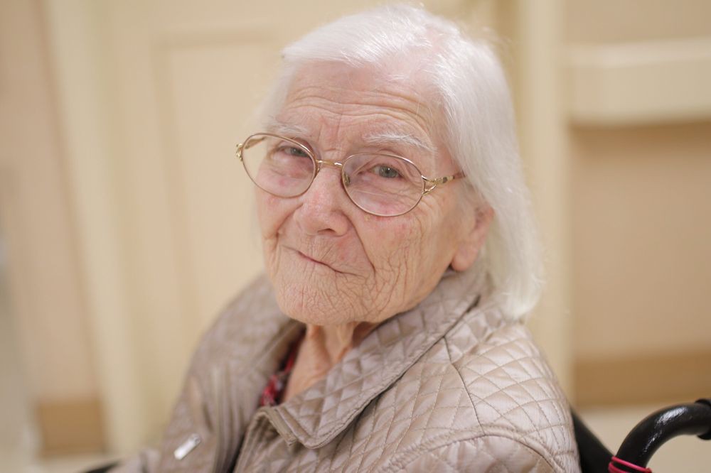 Elderly woman with glasses and white hair smiling softly.