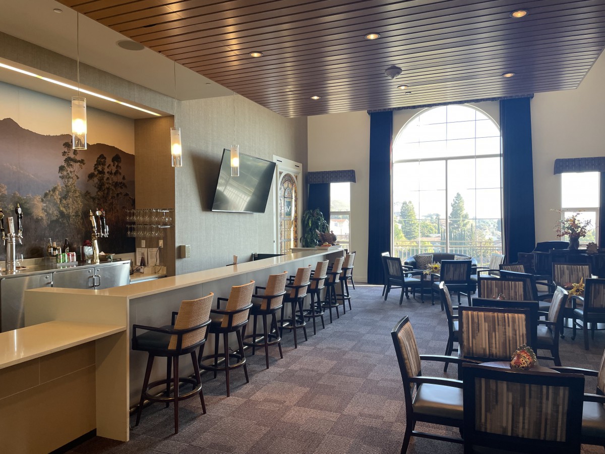 A modern restaurant interior with a bar and seating area, featuring large windows that allow natural light to fill the space.