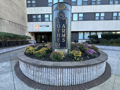 The entrance of Luther Arms, featuring a prominent sign and colorful flower beds.