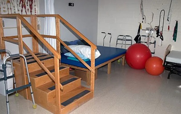 A physical therapy room equipped with stairs, a mat table, crutches, a walker, and an exercise ball.