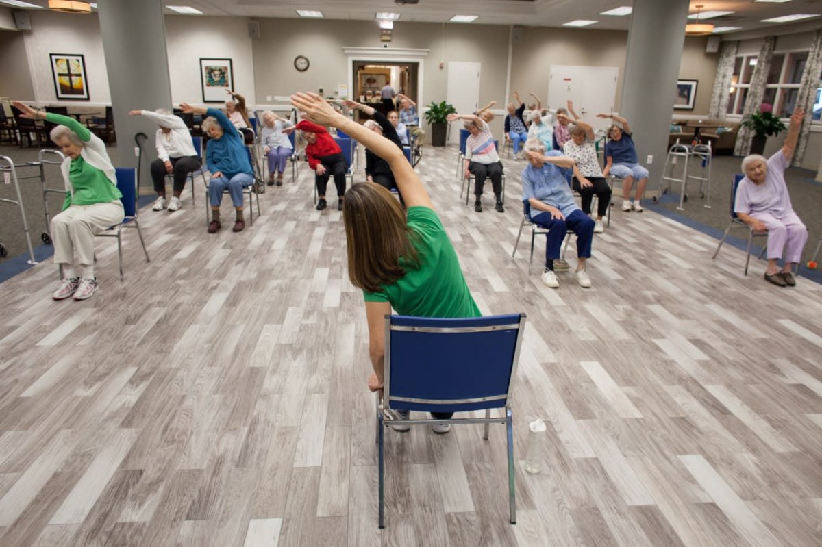 A group of senior citizens participating in a seated exercise class indoors.