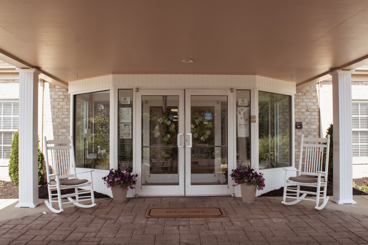 A welcoming entrance with glass doors, flanked by potted plants and rocking chairs.