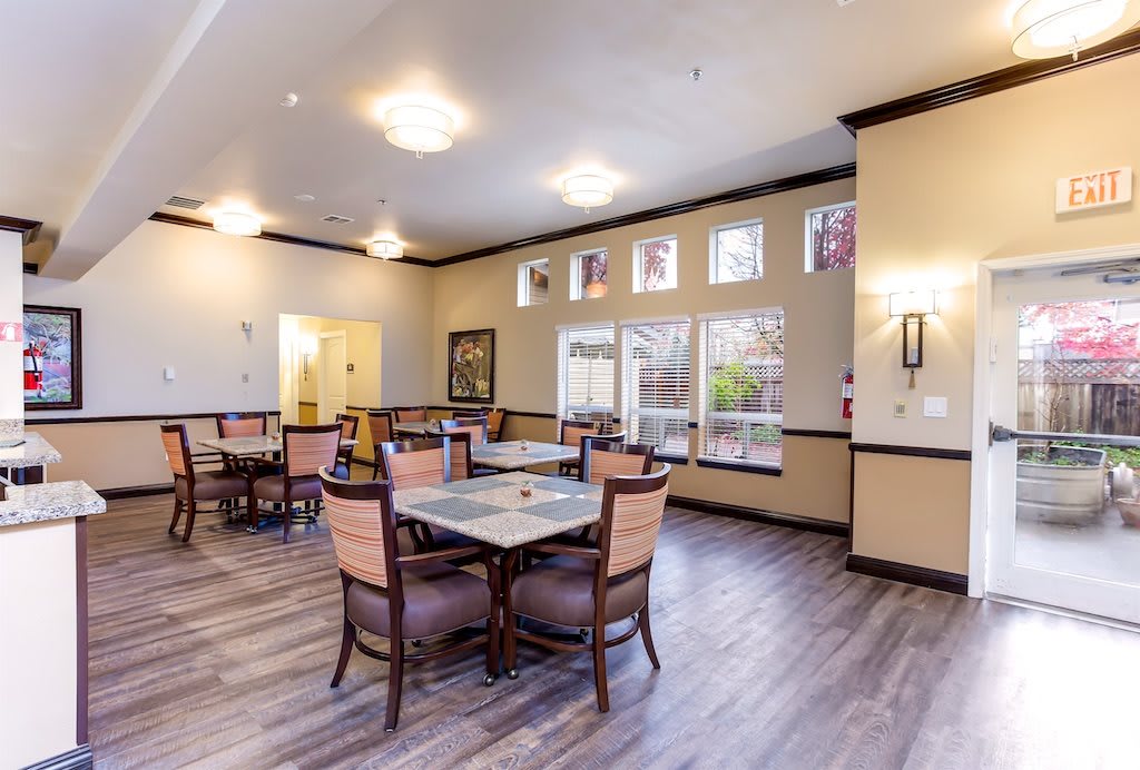 A well-lit dining area with tables and chairs, featuring wood flooring and natural lighting.