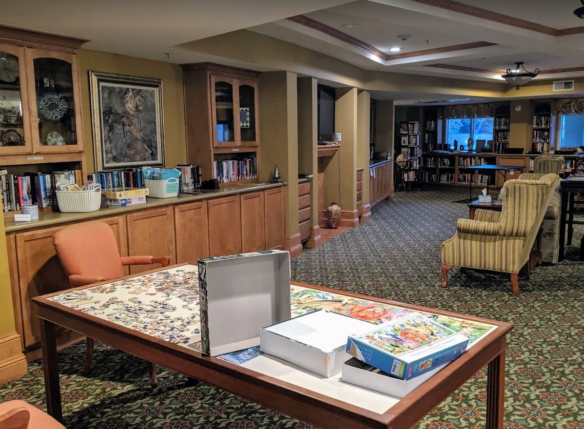 A cozy recreation room with a puzzle on the table and bookshelves in the background.