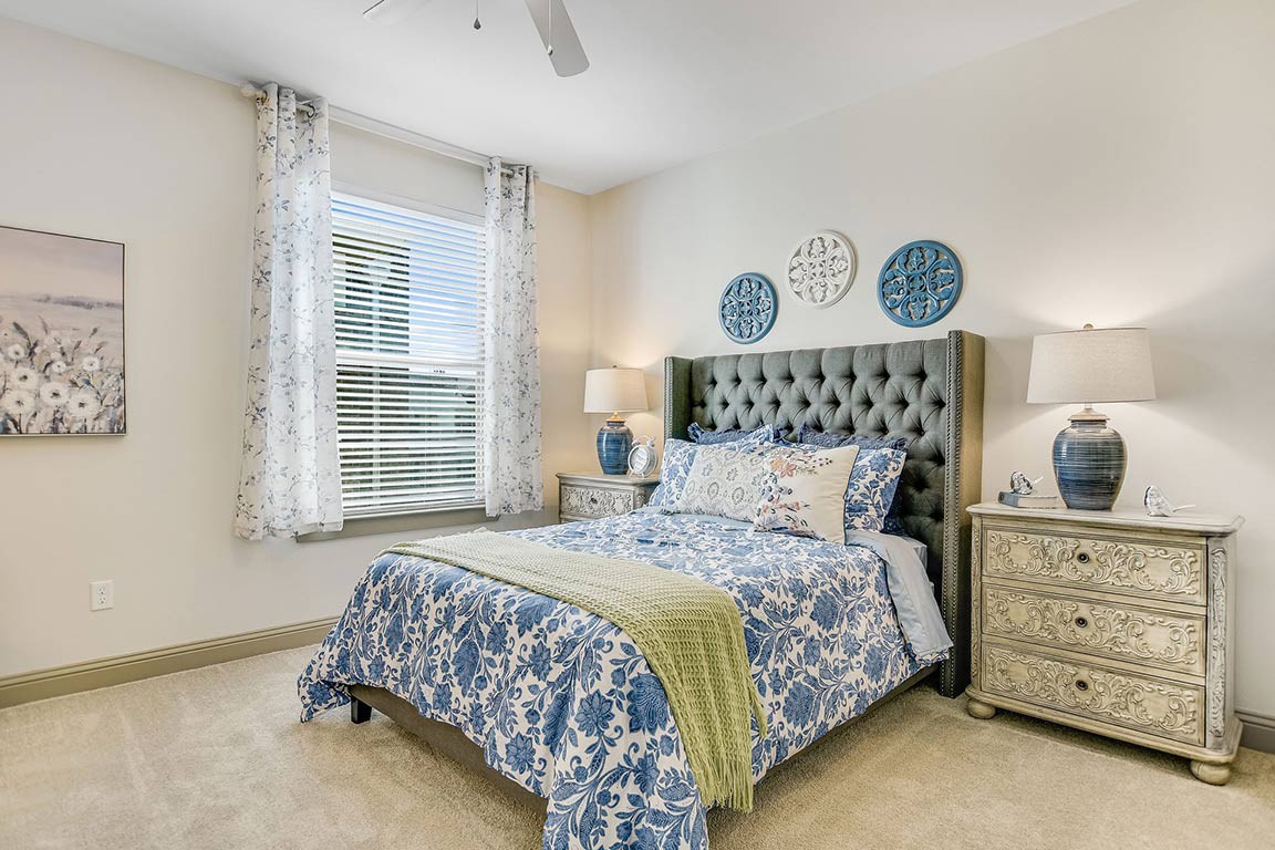 A well-decorated bedroom with blue and white bedding, featuring a tufted headboard, bedside tables with lamps, and decorative wall plates.