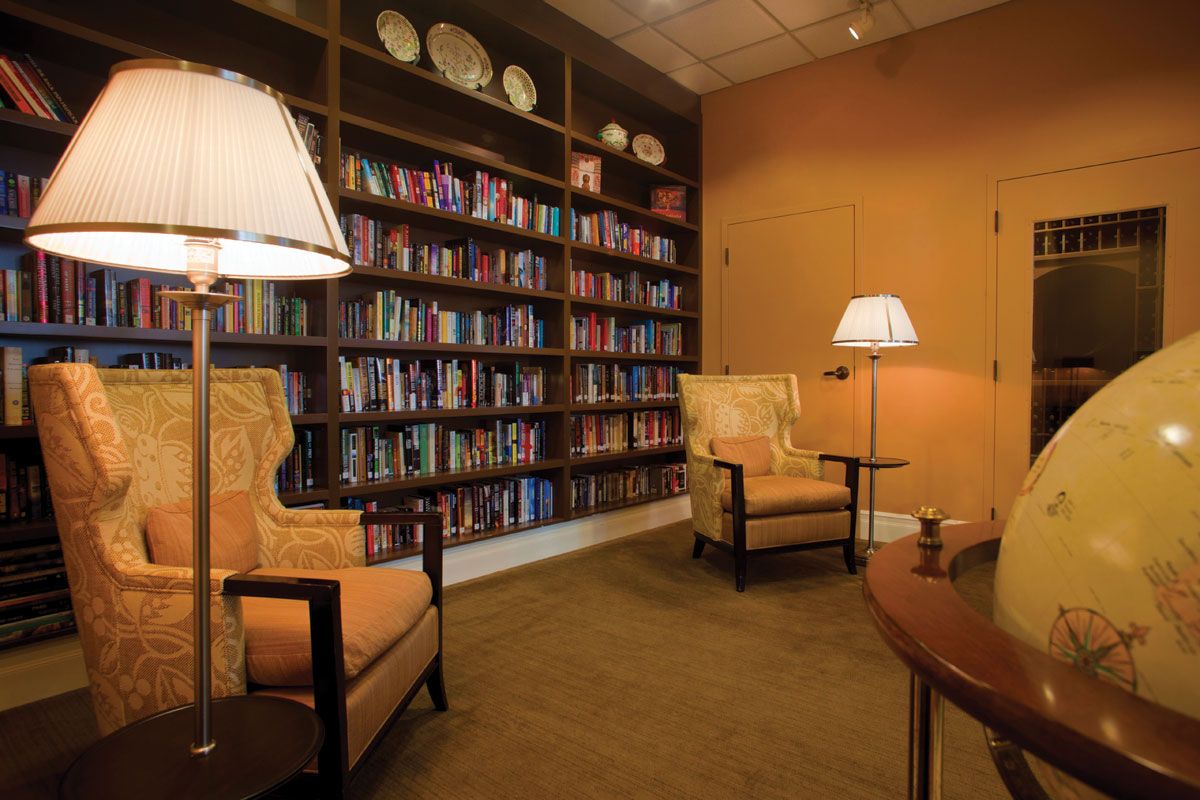 A cozy library with bookshelves, armchairs, and warm lighting.