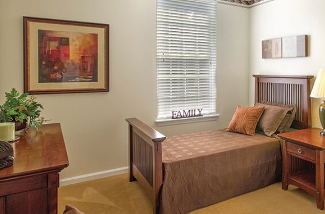 A cozy bedroom with a single bed, a window with blinds, and wall art.