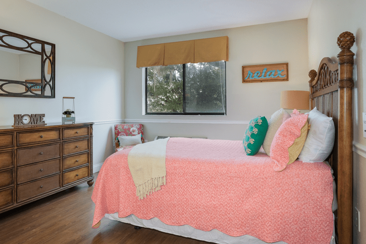 A cozy bedroom with a pink bedspread, colorful pillows, and wooden furniture.