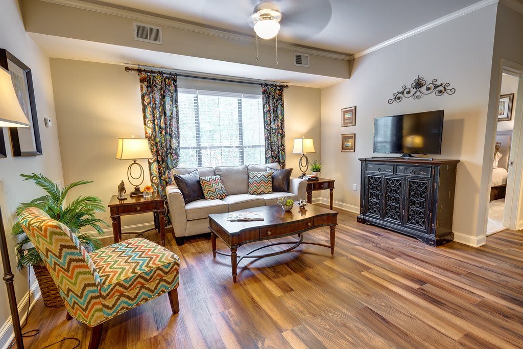 A modern living room with stylish decor, featuring a sofa, coffee table, and a TV, complemented by natural light from a large window.