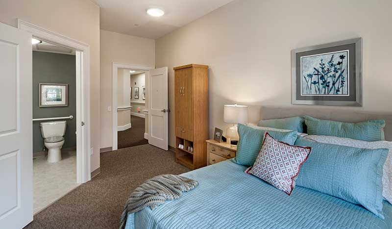A cozy bedroom with a neatly made bed, wooden wardrobe, and soft lighting.
