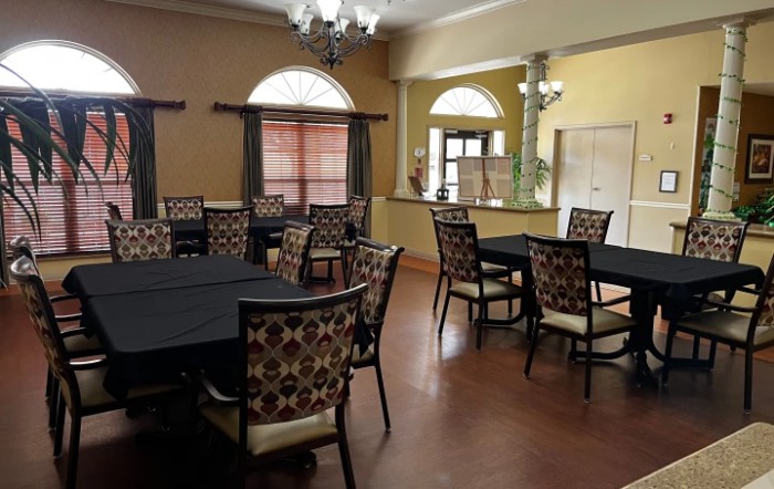 A cozy dining area with round tables and patterned chairs, featuring large windows and warm lighting.