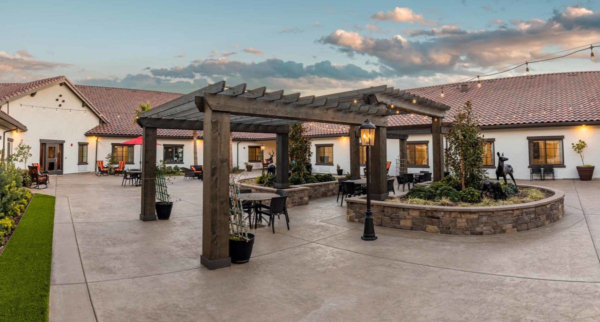 A beautiful outdoor patio with a wooden pergola and seating, set against a sunset sky.