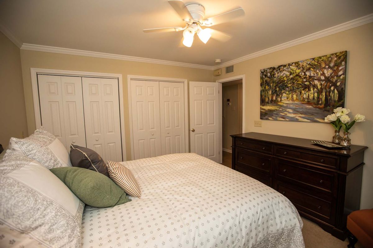 A cozy bedroom featuring a bed with pillows, a large wardrobe, and a dresser under wall art.