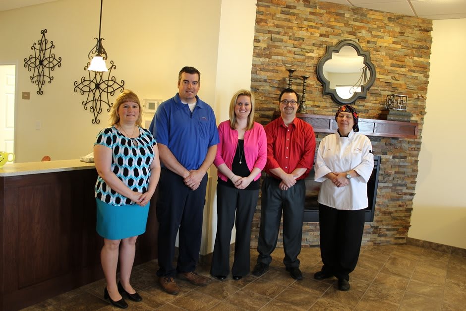 A group of five people posing indoors, wearing casual and professional attire.