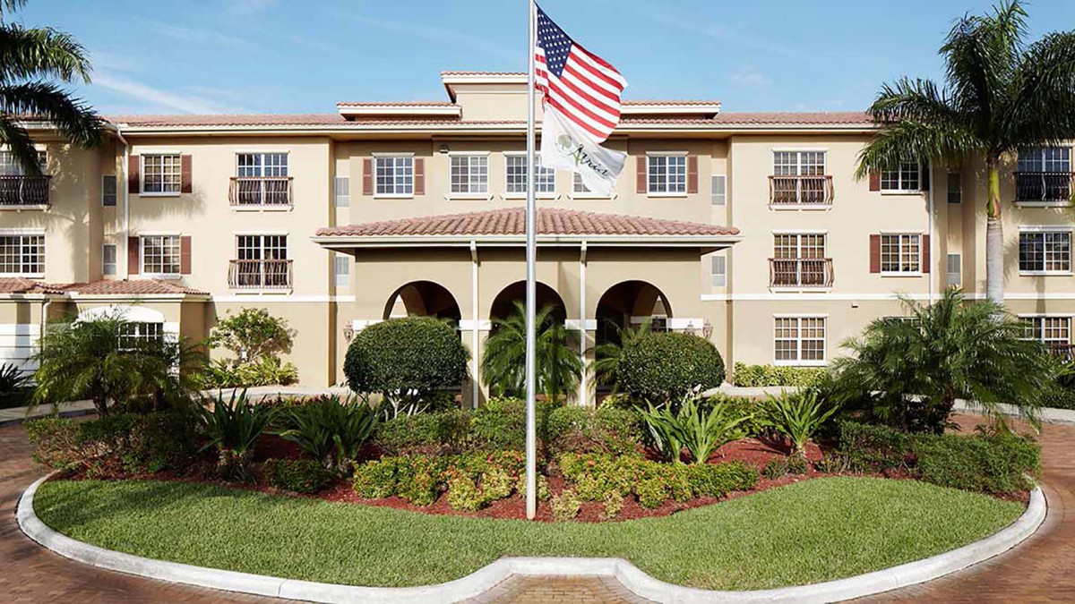 A large building with a U.S. flag in front, surrounded by well-maintained landscaping and trees.