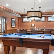 A stylish game room featuring a pool table with blue felt, warm wood paneling, and pendant lighting.