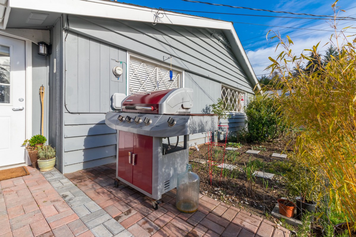 A red and silver barbecue grill on a patio in a backyard garden.