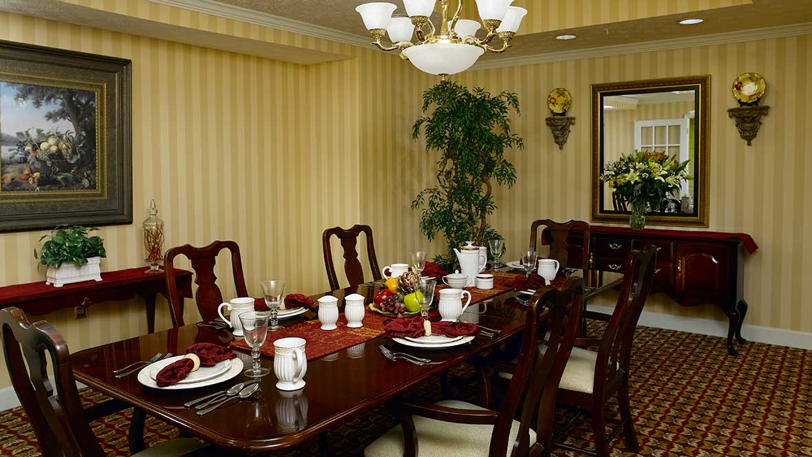 An elegant dining room featuring a formally set table with a chandelier overhead and striped wallpaper.