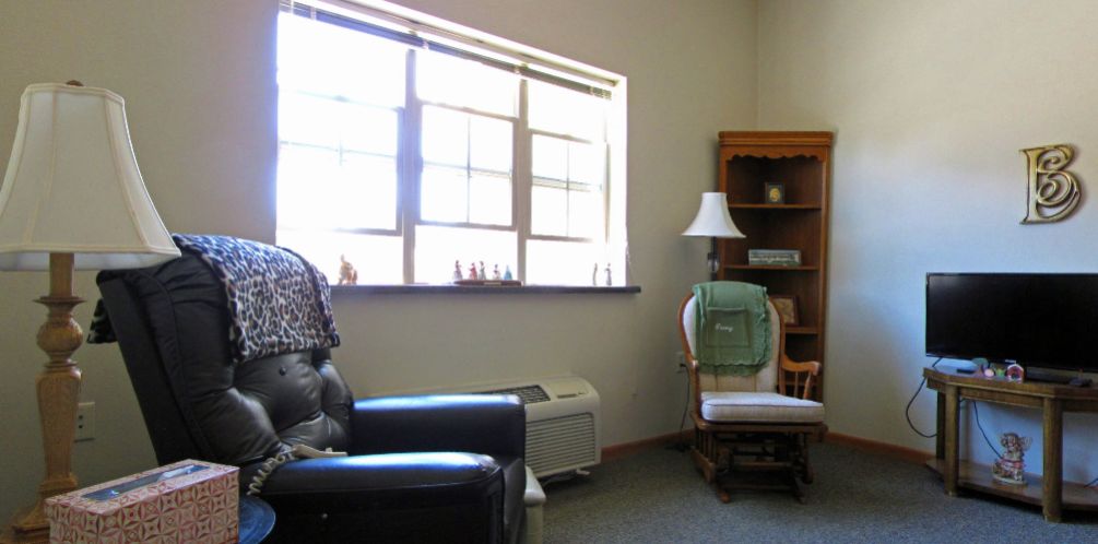 A cozy living room corner with a window, chair, and shelves.