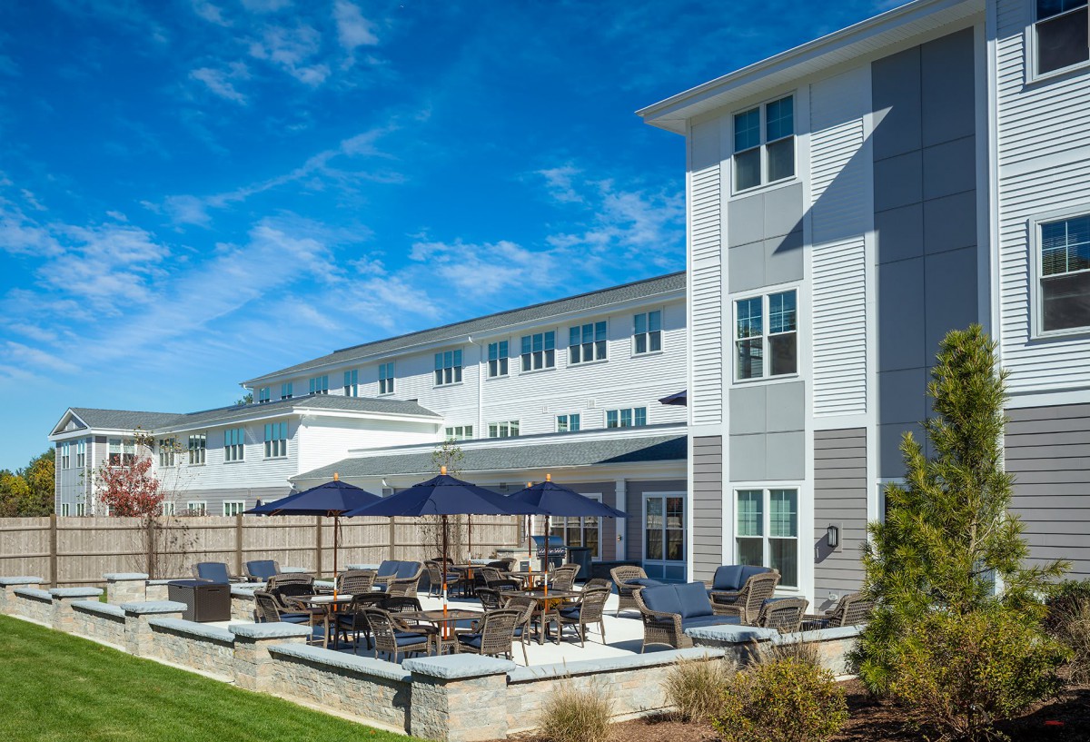 A modern residential building with outdoor patio seating under a clear blue sky.