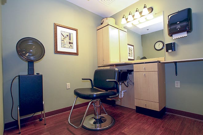 A cozy hair salon setup with a barber chair and mirror under warm vanity lights.