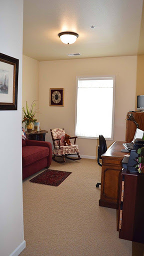 A cozy living room and home office combination with a comfortable sofa, rocking chair, and desk next to a bright window.