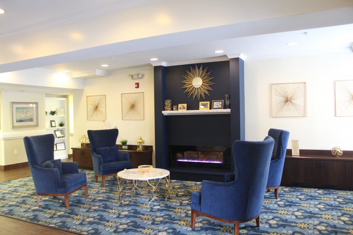 A modern lobby with blue chairs and a decorative fireplace, featuring stylish decor and a patterned carpet.