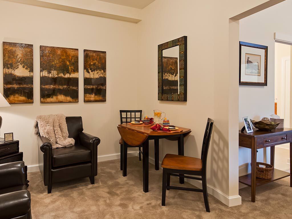 A cozy living room corner with artwork, a small table, and chairs.