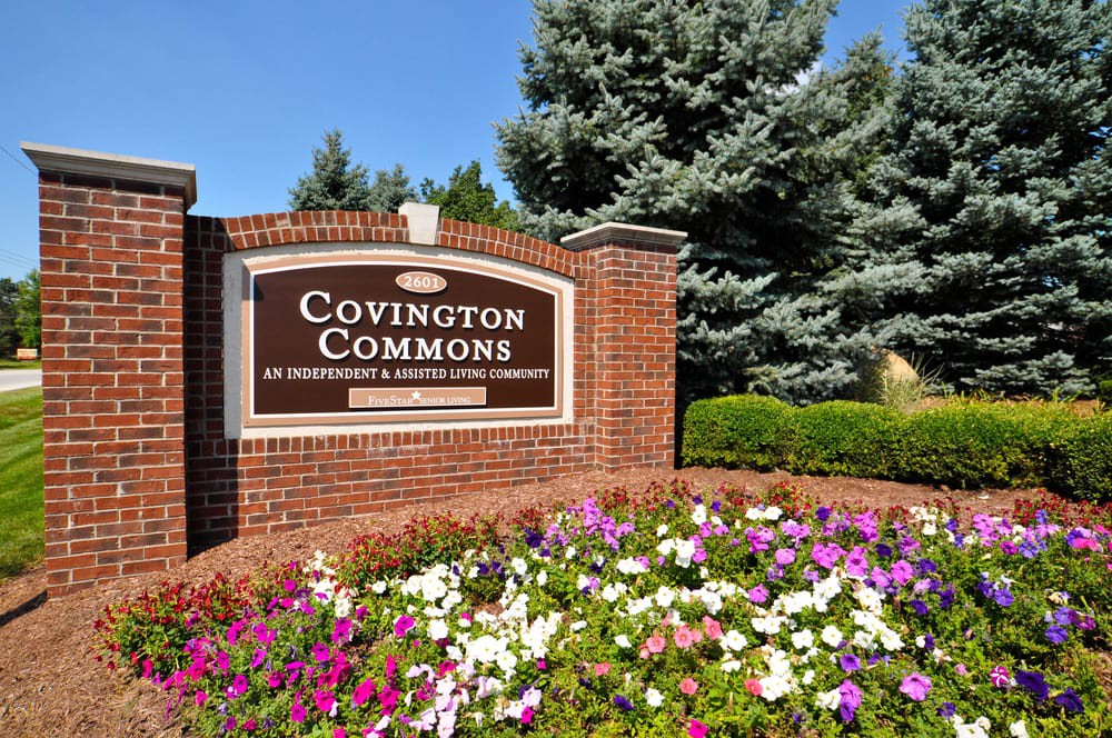 A landscaped entrance sign for Covington Commons surrounded by colorful flowers and greenery.