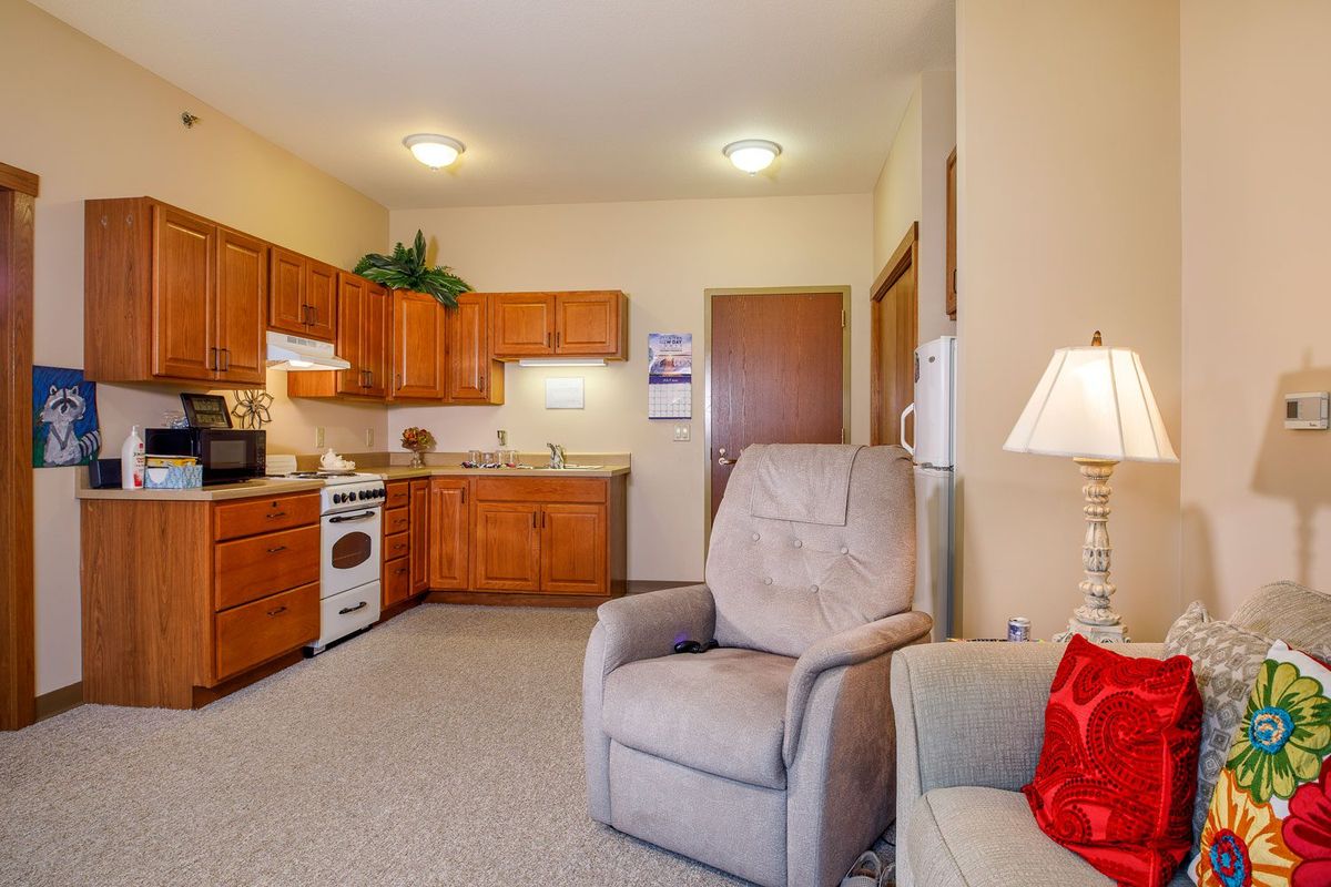 A cozy kitchen and living area with wooden cabinets, comfortable chairs, and a lamp.