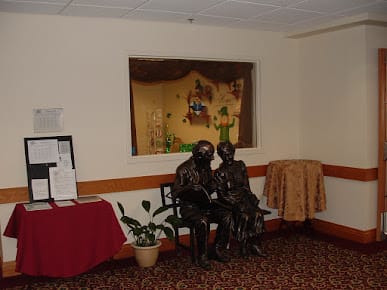 Interior room featuring a sculpture of two figures sitting together, surrounded by artistic decor and plants.