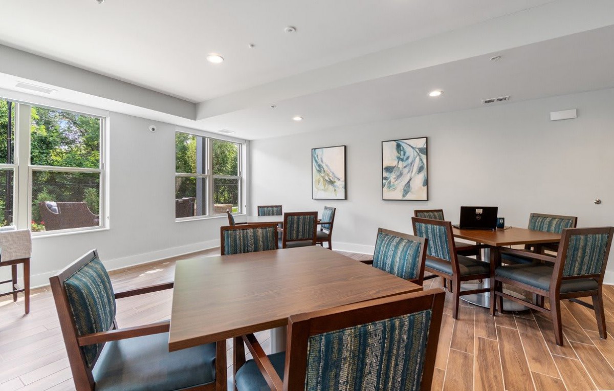 A bright meeting room with wooden floors, tables, chairs, and artwork on the walls.
