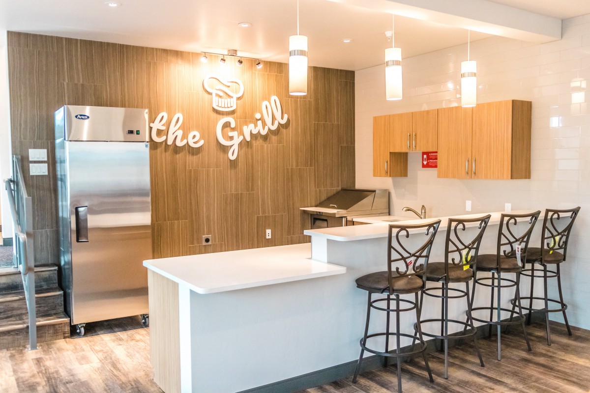 A modern kitchen area with bar stools and a grill setup, featuring stylish wood paneling and pendant lights.