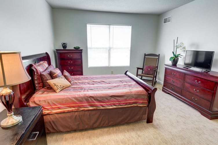 A cozy bedroom with a wooden bed, dresser, and chair, featuring a large window.