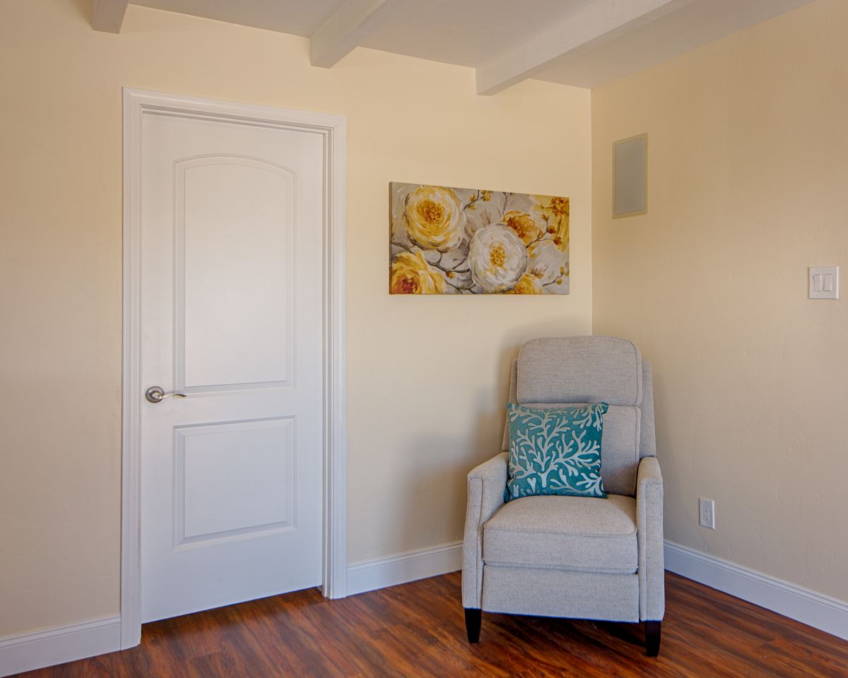 A cozy corner featuring a cushioned chair with a decorative pillow, next to a closed door and floral artwork on the wall.