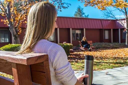 A tranquil autumn day where one person enjoys their beverage while seated on a bench, and another relaxes in the background.