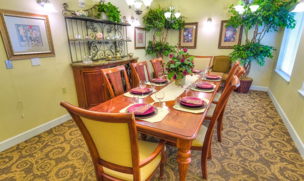 A well-decorated dining room with a wooden table and chairs, set for a meal with elegant place settings and surrounded by greenery.