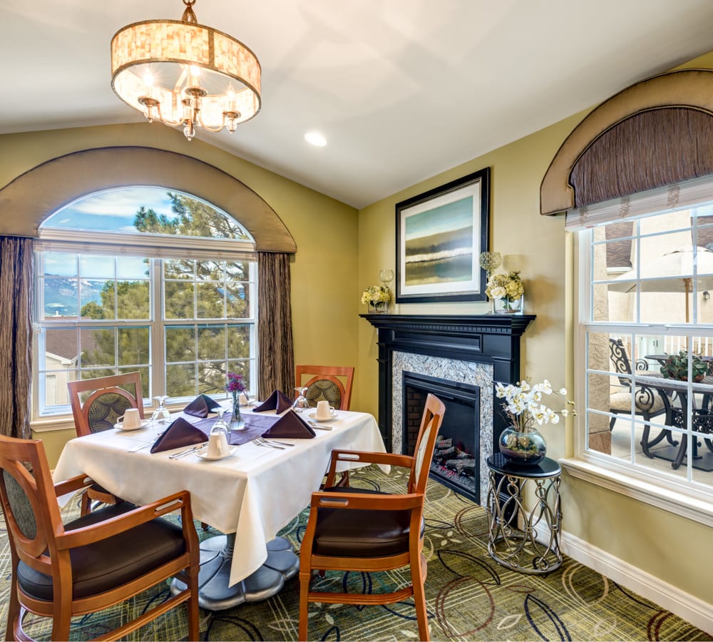 A cozy dining room with a table set for four, featuring a chandelier and a fireplace.