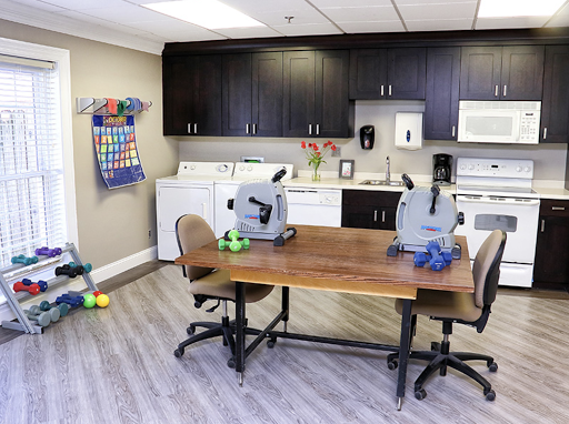 A multifunctional room featuring a kitchenette area with laundry facilities, therapy equipment, and a workspace.